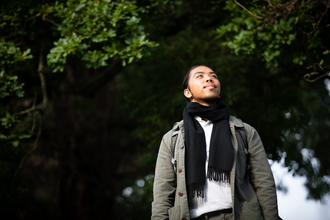 A young person looks up into the sky with woodland in the background