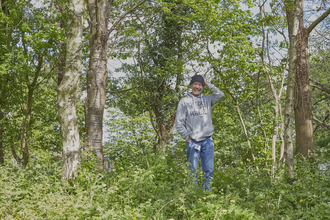 A volunteer stands in a woodland with a smile on his face