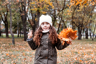 A girl stands in an autumnal park, holding a handful of autumn leaves