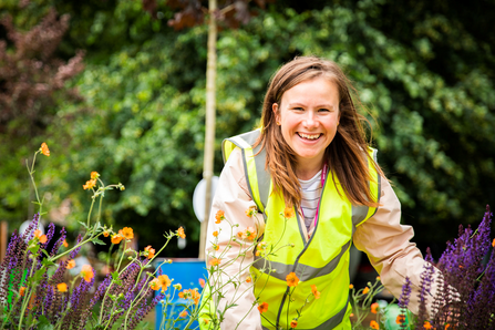 Zoe Claymore - Garden Designer planting in a high vis jacket with organe flowers in the foreground