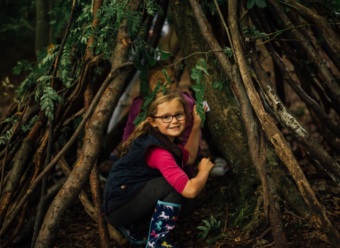 A young girl looks back smiling as she plays in a wooden shelter, the Wildlife Trusts