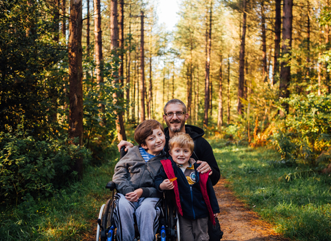 Two boys, one a wheelchair user, and their dad on a woodland path