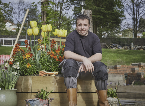Colourful spring bulbs in pots with a man sitting next to them and smiling