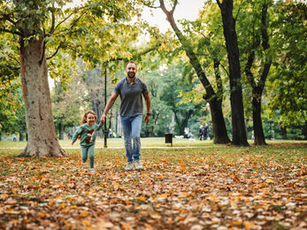 father and daughter walking through a park surrounded by leaves