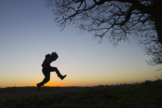 A silhouette of a child playing outdoors at sunset, The Wildlife Trusts