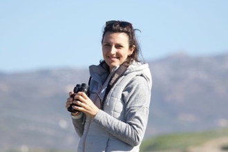 Natalie White stood holding a pair of binoculars with hills in the background