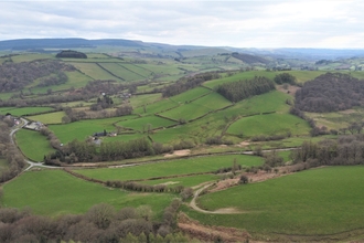 Aerial photograph of the Pentwyn Farm in Wales, showing rolling hills with patches of woodland and an overcast sky