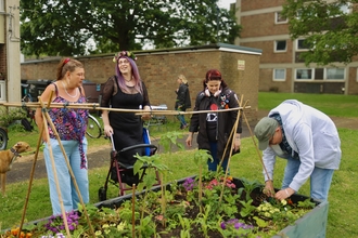 Four people around a planter of veg and flowers in a housing estate