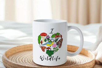 A mug saying I heart wildlife. The heart made up of illustrated wildlife, including a blue tit, butterfly, mushroom, moth and leaves