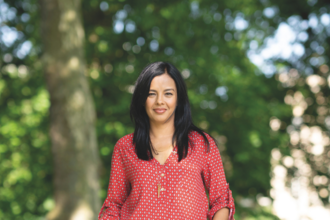 Liz Bonnin standing facing the camera and smiling. Behind her can be seen trees in soft focus