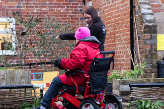 A wheelchair user with a Wildlife Trust staff member, in an urgan garden looking at raised beds