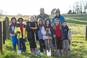 A group of school children with spades, smiling at the camera after planting trees