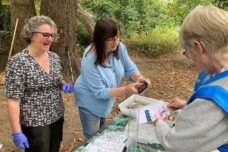 Three women outside in woods around a table examining paperwork