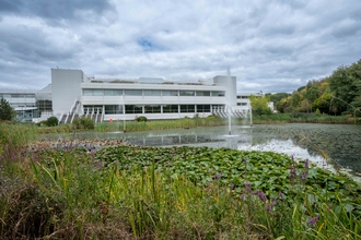 The Nationwide building, a large white building, in the background. In front of the building is a large lake with greenery surrounding it