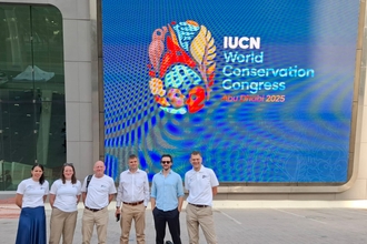 A team of six people from The Wildlife Trusts stand in front of the IUCN World Conservation Congress sign, smiling at the camera