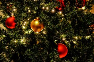 Red and gold baubles hanging on a christmas tree that's covered in fairy lights