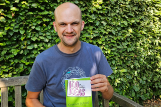 Man holding green book on a bench