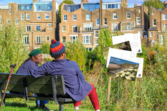 Two men talking on a bench overlooking terraced housing, and superimposed postcard images