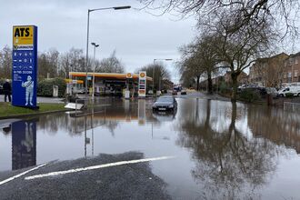 Flooding seen in a car park, with flats on the right hand side and a fuel station behind