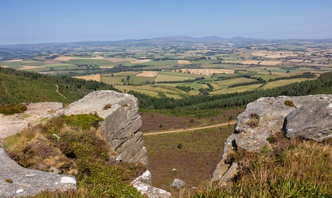 A sweeping view of the Rothbury Estate, from the Simonside Hills. A gap in a rock formation shows a vast area of field, out to the horizon and blue sky