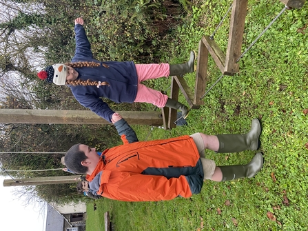 Older child helping younger child to walk along obstacles made from wood