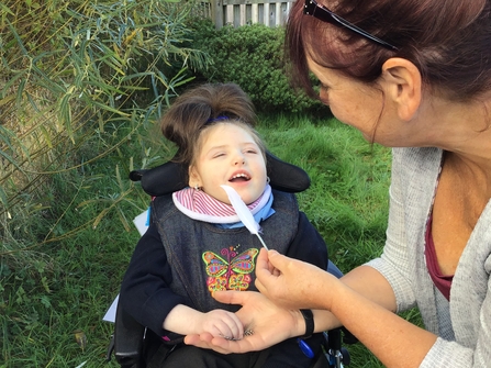 Child in wheelchair looking at a feather