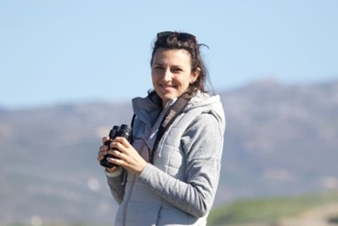 Natalie White stood holding a pair of binoculars with hills in the background