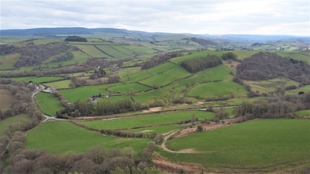 Aerial photograph of the Pentwyn Farm in Wales, showing rolling hills with patches of woodland and an overcast sky