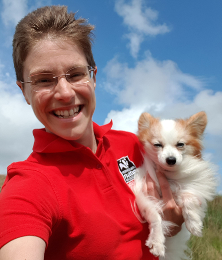 Tammy from Montgomeryshire Wildlife Trust stands outside on a sunny day, holding her papillon dog Cerrig