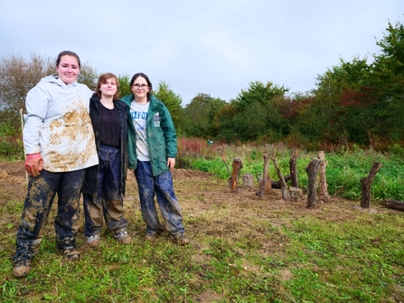 Three young people in muddy clothes in a green area.