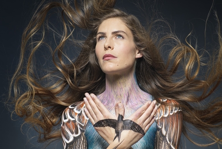 Hannah has been painted with wings across her shoulders and a swift on her hands. Her hair is blowing in the wind and she is staring into the distance