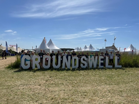 Wildlife Trust staff standing in front of a big Groundswell sign. Behind them can be seen bell tents
