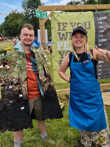 A person wearing the peat bog poncho, which has layers of handmade felt, paint, and beautiful embroidery invoking the peatland habitat