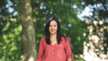 Liz Bonnin standing facing the camera and smiling. Behind her can be seen trees in soft focus