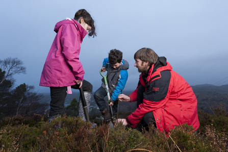 Two children and an adult planting trees