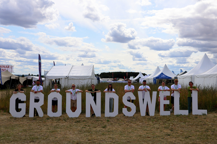 Members of The Wildlife Trusts' team stand behind the individual letters of a Groundswell sign, smiling at the camera
