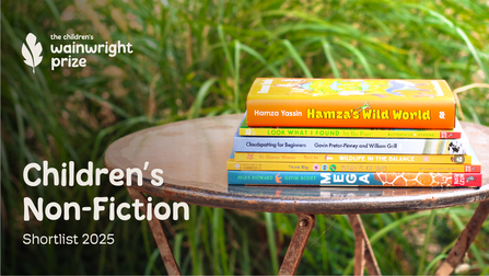 A pile of books shortlisted for the Wainwright Prize for Children's Non-Fiction 2025 sit on an outside table. In order from top to bottom the books are: Hamza's Wild World by Hamza Yassin, Look What I Found by the River, Cloudspotting for Beginners by Gavin Pretor-Pinney and William Grill, Wildlife in the Balance by Dr Sharon Wismer and Terri Po, Secrets of Bees by Ben Hoare and Nina Chakrabarti and MEGA by Jules Howard and Gavin Scott