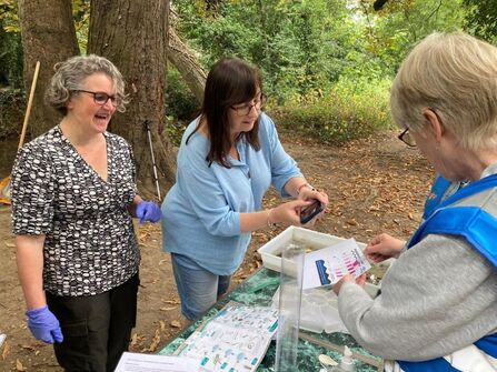 Three women outside in woods around a table examining paperwork