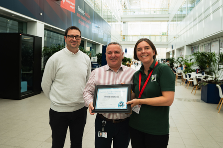 Two members of staff from Nationwide are presented with the Biodiversity Benchmark certificate by the Chief Executive of Wiltshire Wildlife Trust, Joanna Lewis. All three are smiling at the camera