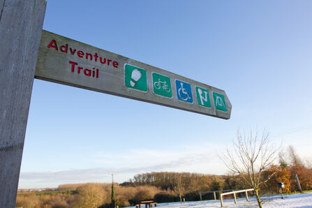 A wooden sign pointing right with the words Adventure Trail and accessibility symbols