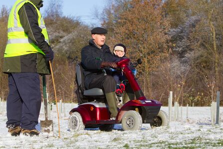 Three people outside in snowy rural scene, one man on a red scooter