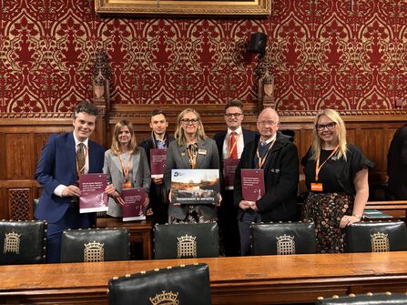 A group of people from The Wildlife Trusts are standing in a room in parliament smiling at the camera. They are holding up copies of a report titled Why the Nuclear Regulatory Review is flawed - and how it could turn the nature crisis into a catastrophe. They are also holding an A3 poster which reads Investment in nature = Investment in security