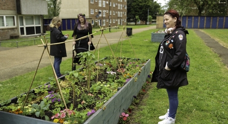 three people standing around a raised bed filled with flowers.