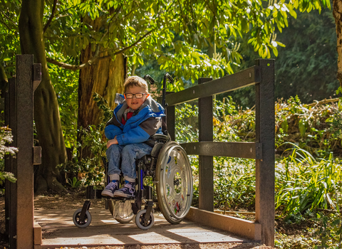 A young boy sitting in a wheelchair on a bridge