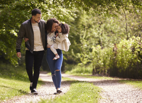 A family walking on a nature trail path. The man has his arm around the woman who is carrying the little girl.