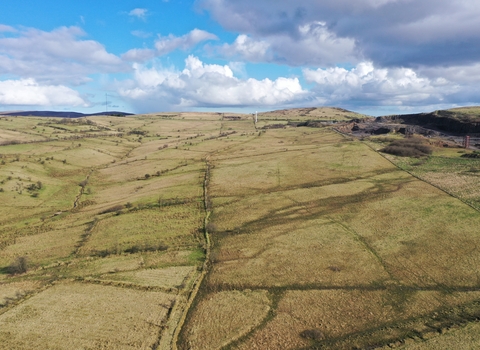 An aerial photograph of Slievenacloy in the Belfast Hills, interlinking grass fields with blue sky and large white clouds above