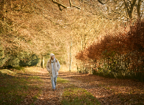A woman walking in autumn colours, wearing a wooly hat and scarf