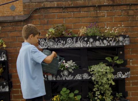 Boy in school uniform waters plants in a repurposed crate planters