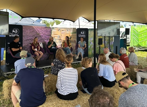 A panel of four women and a man sitting on a stage at Groundwell with Wildlife Trust banners behind them. Facing them, the audience is sitting on hay bales