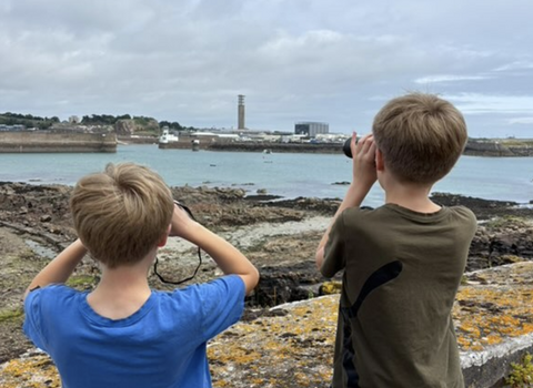 Two young boys look out at sea with binoculars